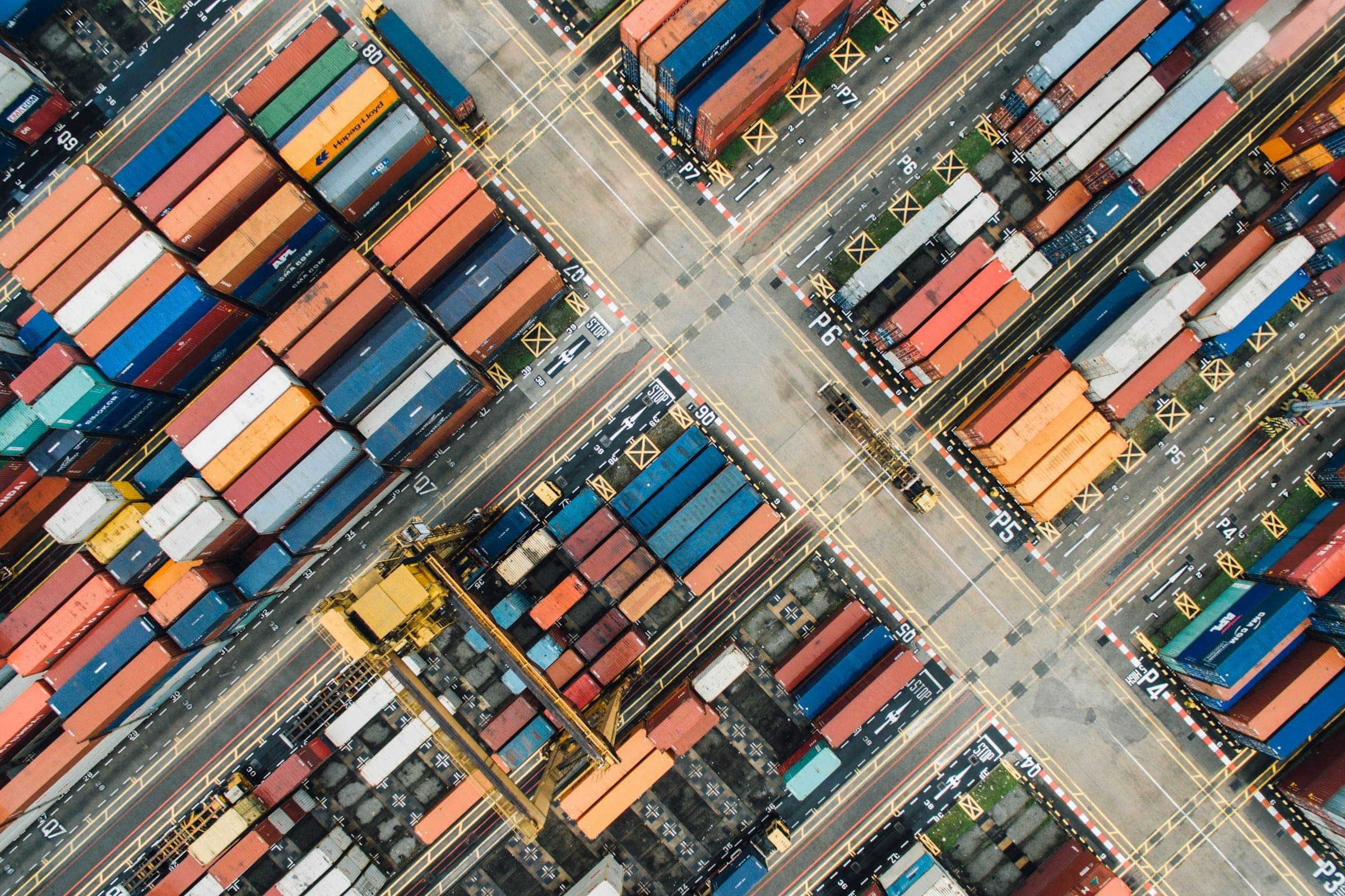 Aerial view of a container terminal with rows of stacked shipping containers and a gantry crane